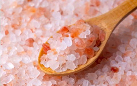 Na zdjęciu drewniana łyżeczka obok piramidki z różowej soli